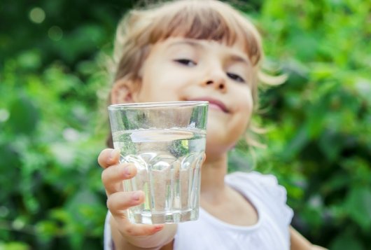 Glimlachend kind steekt een glas met water vooruit